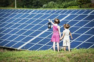 Children standing together in front of solar panels, girl holding old-fashioned latern